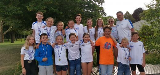 Gruppe junger Schwimmerinnen und Schwimmer mit Medaillen und Trainer