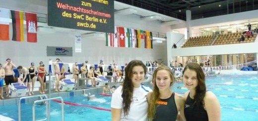 drei Schwimmerinnen lachen in die Kamera - im Hintergrund Schwimmbahnen