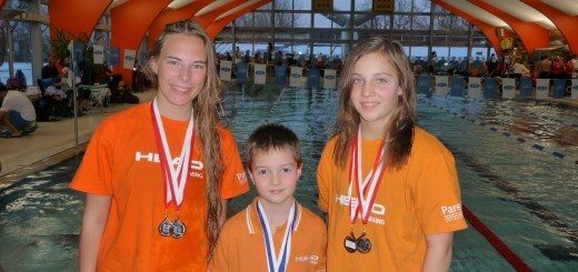 zwei Schwimmerinnen und ein Schwimmer mit Medaillen lachen in die Kamera