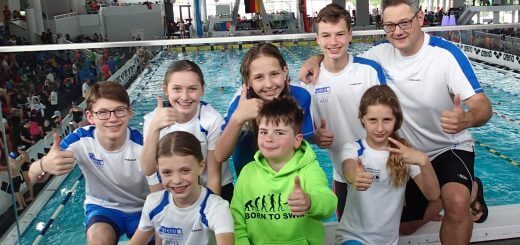 Gruppe junger Schwimmerinnen und Schwimmer mit Trainer zeigen Daumen nach oben